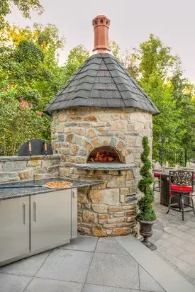A stone oven with a slate roof is sitting next to a kitchen.