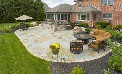 A large patio with furniture and an umbrella in front of a brick house.