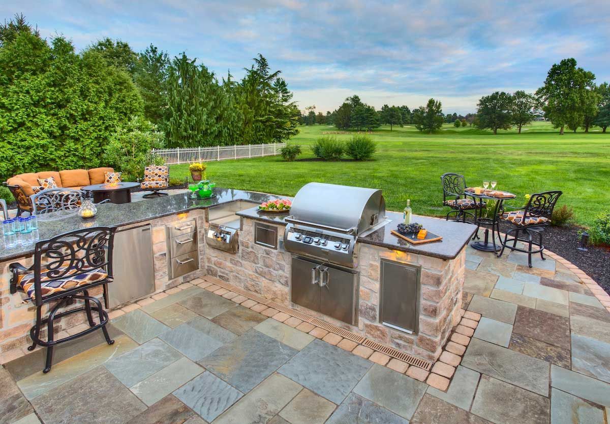 A large outdoor kitchen with a grill and a table and chairs.