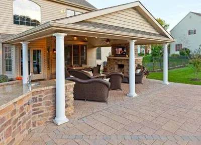 A house with a covered patio with chairs and a fireplace.