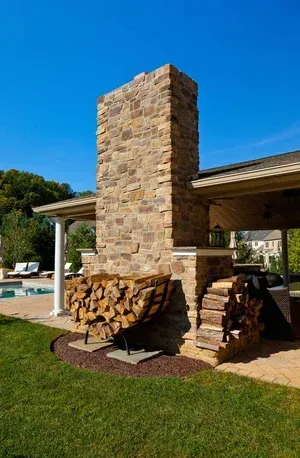 A large stone chimney is sitting next to a pile of logs.