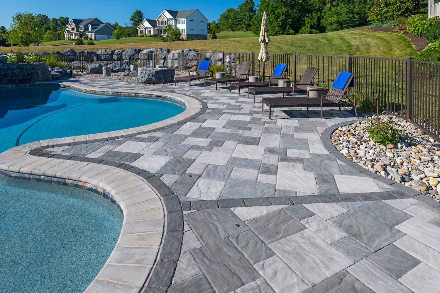 A large swimming pool with a patio and chairs around it.
