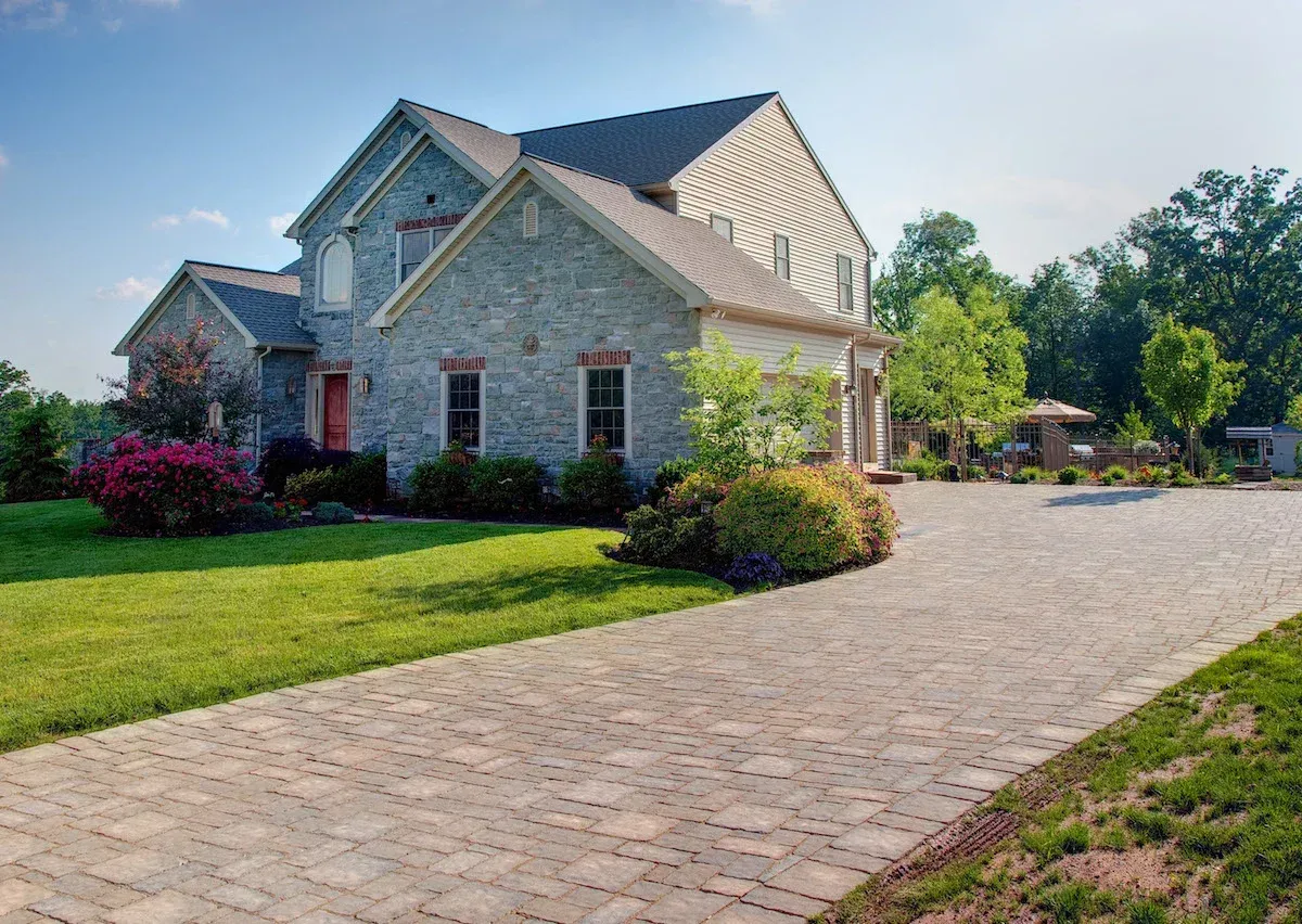 A large stone house with a brick driveway in front of it.