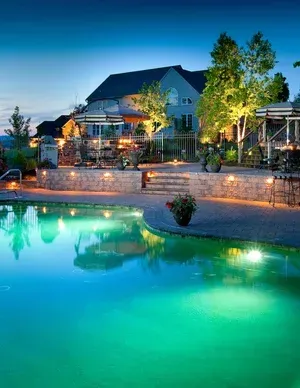 A large swimming pool is lit up at night in front of a house