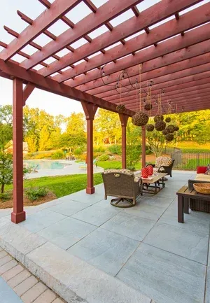 A patio with a pergola and a swimming pool in the background.