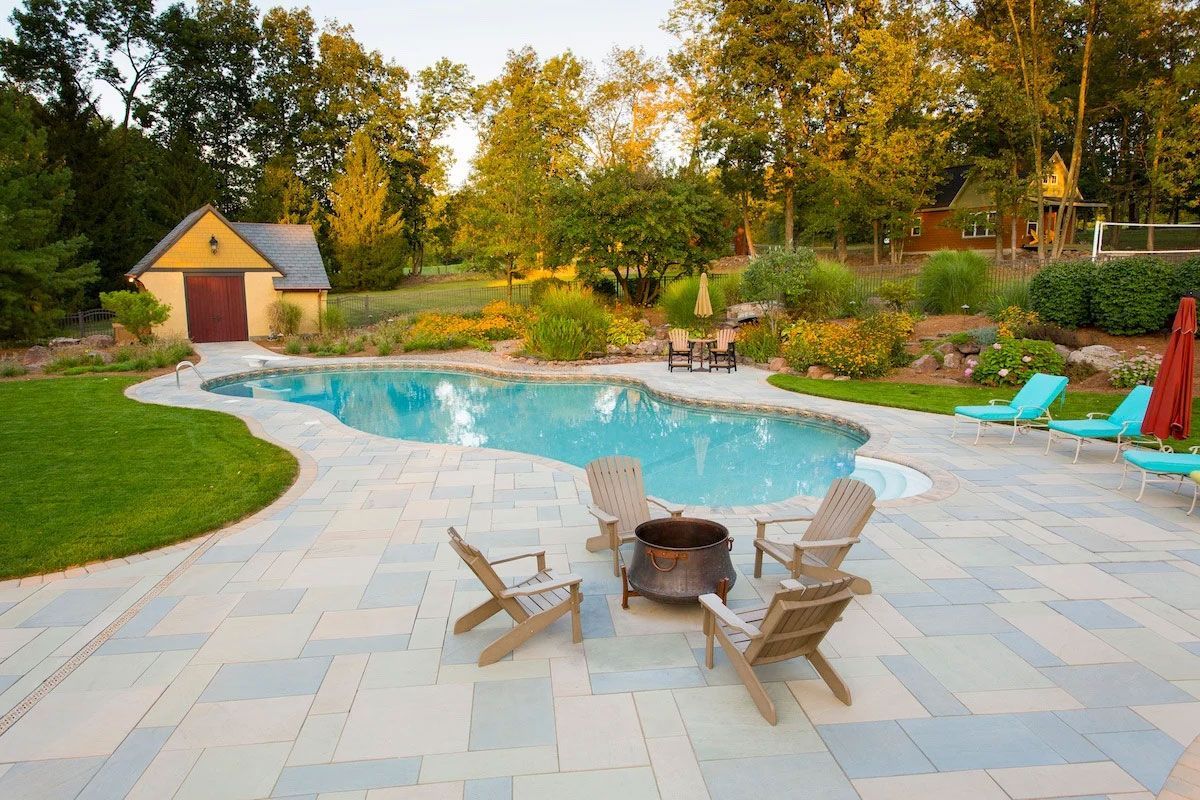 A patio with chairs and a fire pit in front of a large swimming pool.