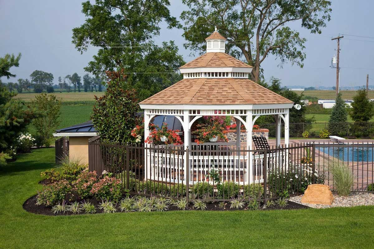 A gazebo is sitting in the middle of a lush green yard next to a pool.