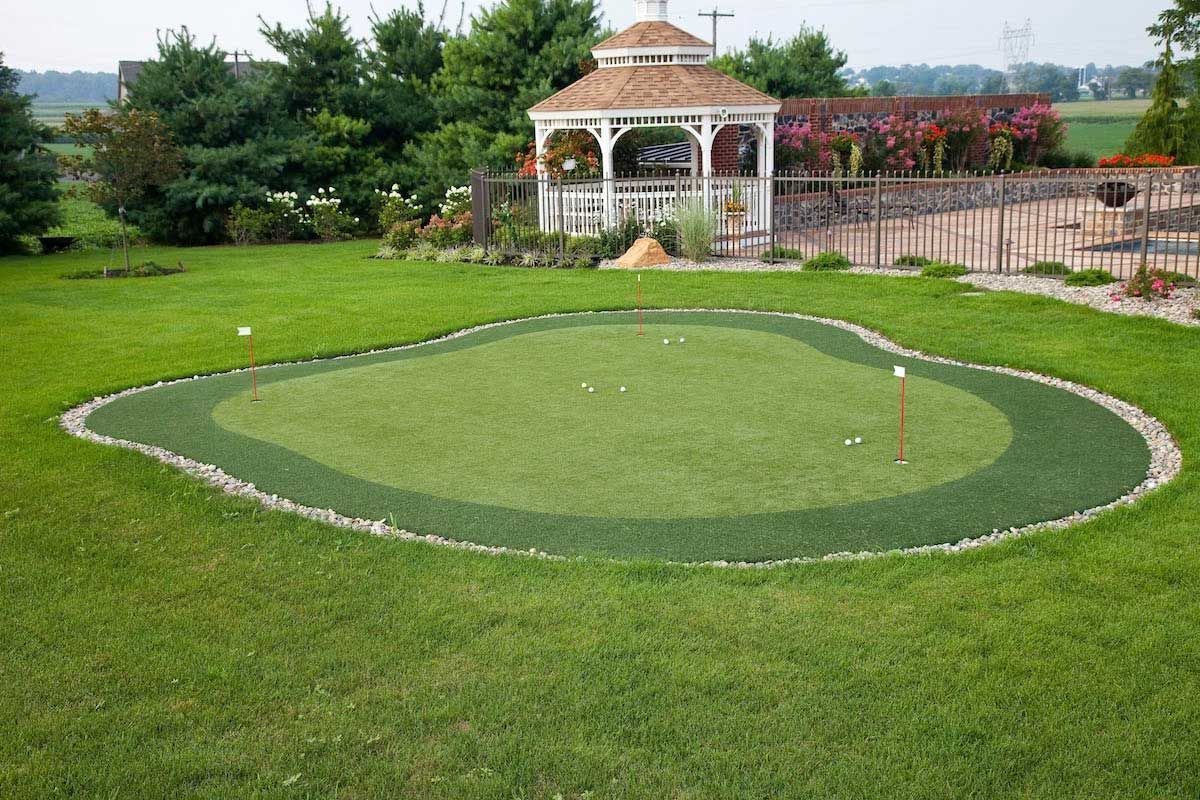 A putting green surrounded by rocks and grass, with a gazebo in the background.