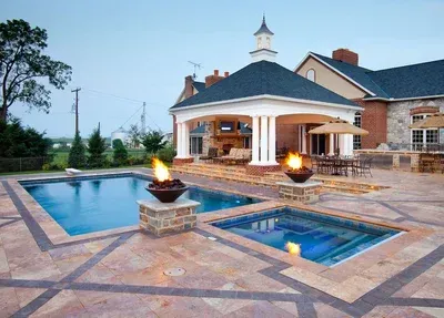 Luxurious backyard with a pool, spa, fire features, and a covered patio connected to a large house.