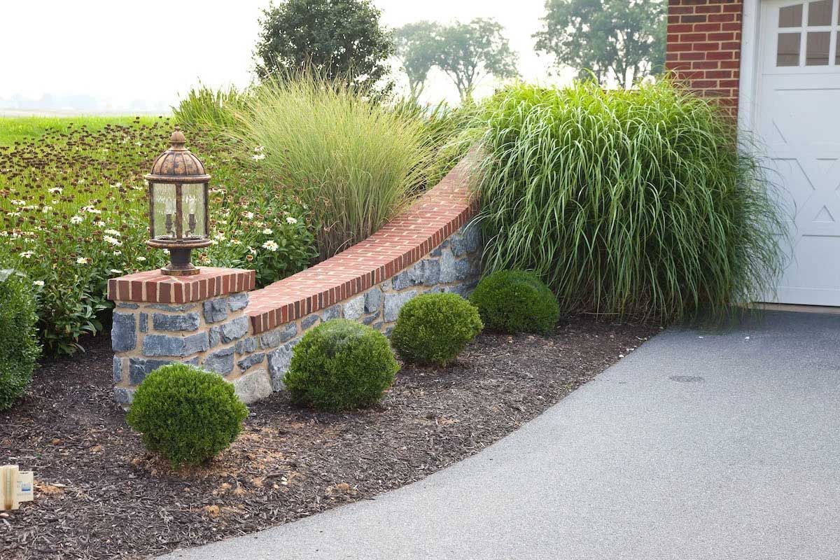 A white garage door is sitting next to a stone wall and bushes.