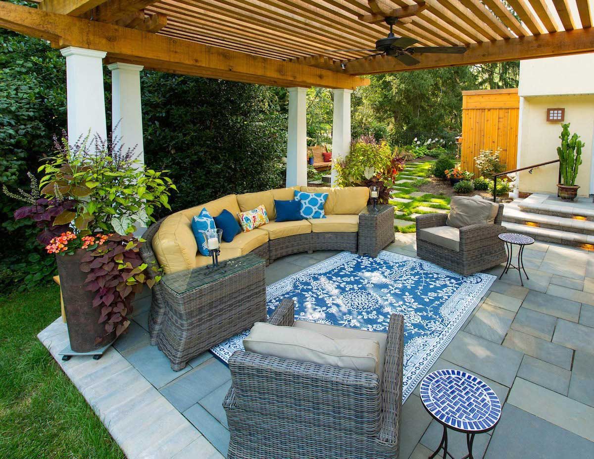 A patio with a couch , chairs , and a rug under a pergola.