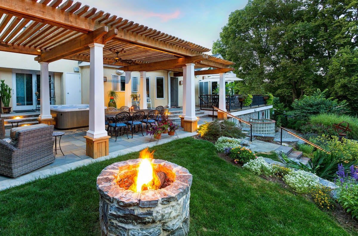 A fire pit in the middle of a lush green yard under a pergola.