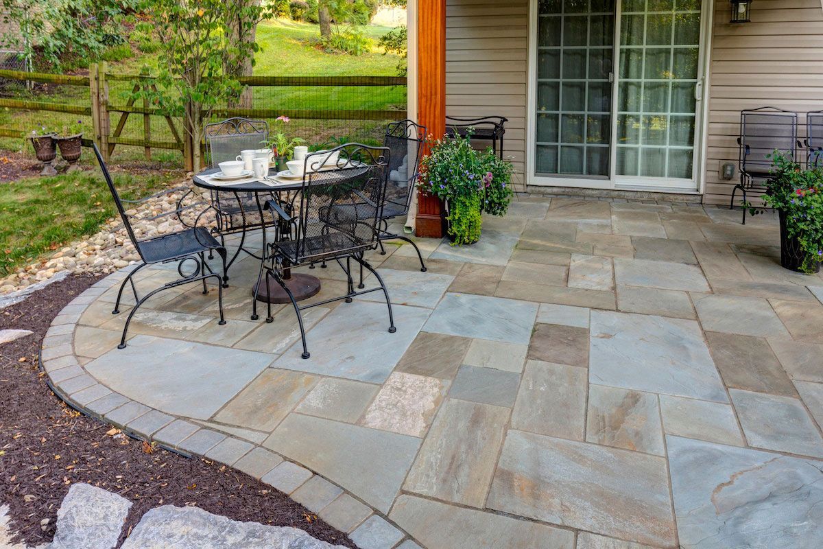 A patio with a table and chairs on it in front of a house.