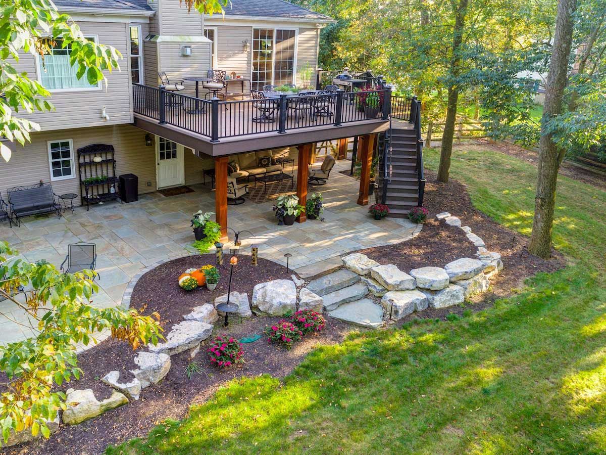 An aerial view of a house with a large deck and patio surrounded by trees.
