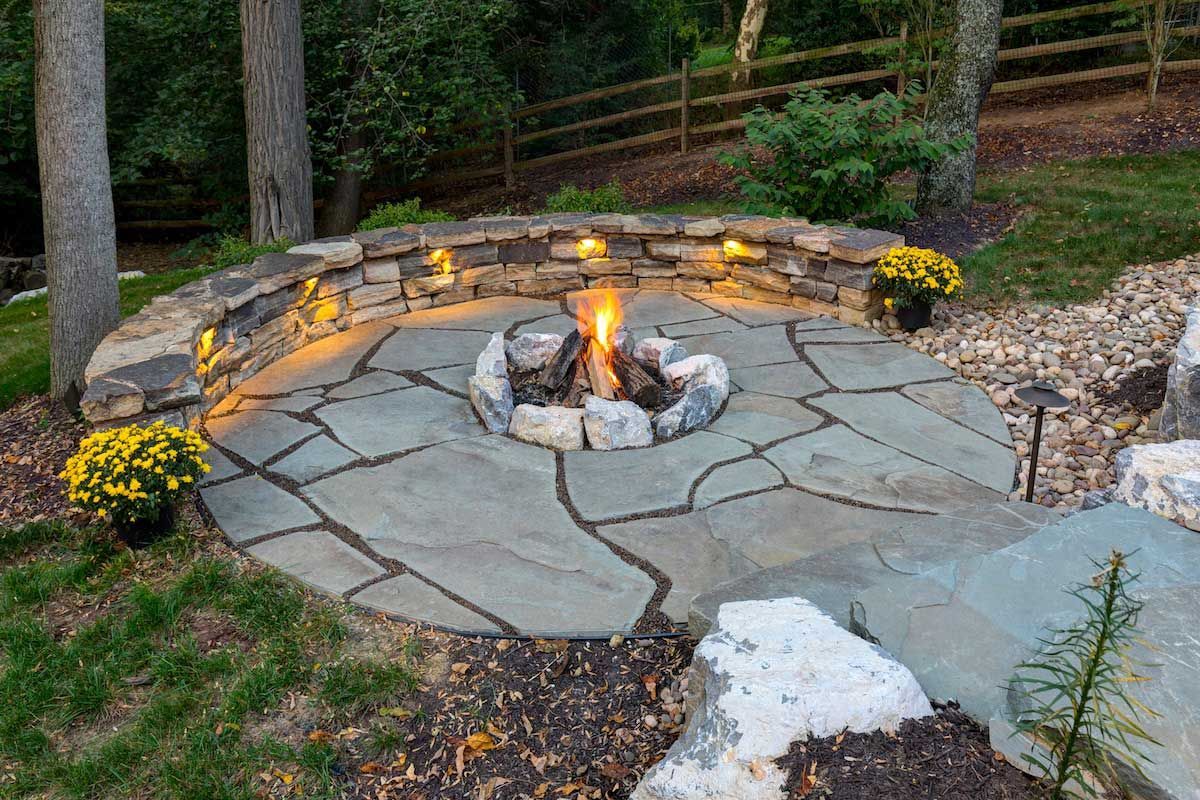 A fire pit is surrounded by rocks and flowers in a backyard.