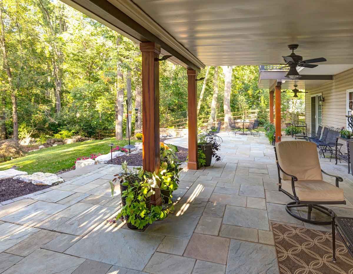 A patio with a ceiling fan and chairs under a covered porch.