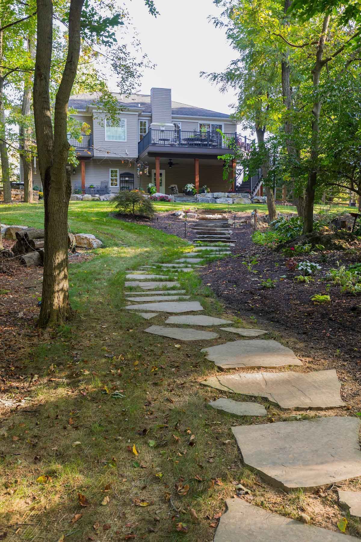 A stone walkway leading to a house in the woods.
