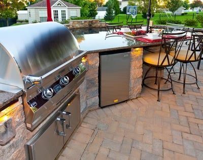 A stainless steel grill is sitting on a brick patio next to a table and chairs.