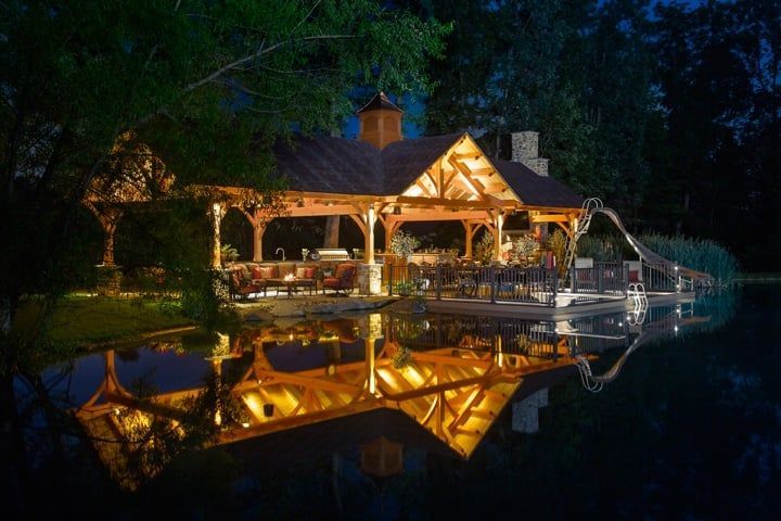 A gazebo is lit up at night and reflected in the water