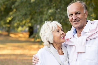 An elderly couple standing next to each other in a park.