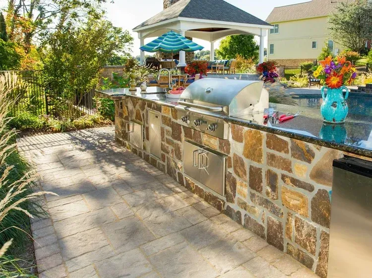 An outdoor kitchen with a grill and a gazebo in the background.