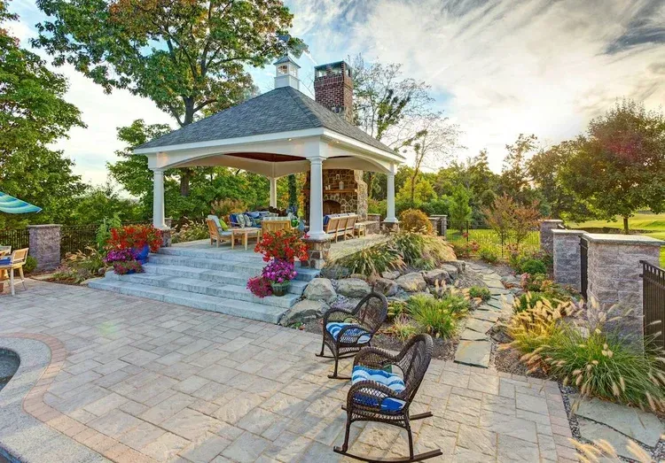 There is a gazebo in the backyard with rocking chairs in front of it.