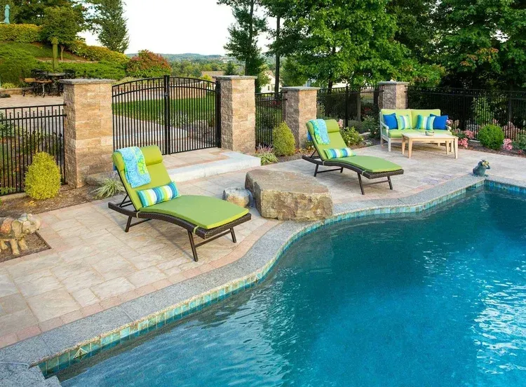 A swimming pool surrounded by lawn chairs and a fence.