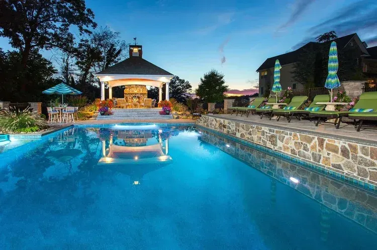 A large swimming pool surrounded by chairs and umbrellas with a gazebo in the background.