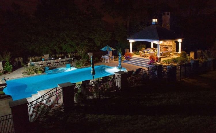 A large swimming pool is lit up at night in a backyard.