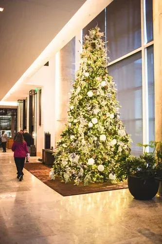 A tall, decorated Christmas tree in a well-lit lobby. A person walks by.