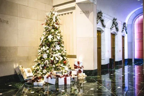 Christmas tree and gifts in a lobby with decorated doorways and reflective marble floor.