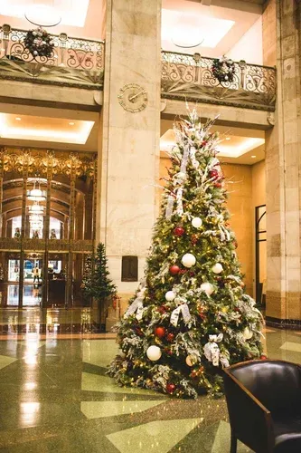 Lobby with Christmas tree, ornate architecture, and reflective floor. Wreaths hang on balcony.