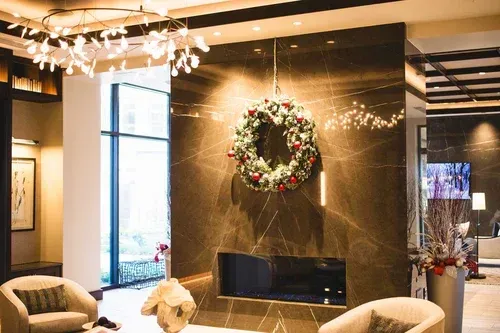 A modern hotel lobby with a fireplace decorated for Christmas; a wreath hangs on a dark marble wall.