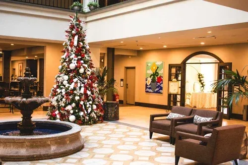 Hotel lobby with Christmas tree, fountain, seating, and art. Beige walls, red/white tree decor.