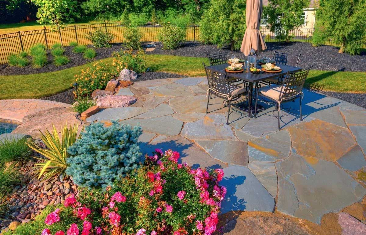 A patio with a table and chairs and an umbrella in a garden.