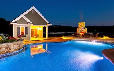 A large swimming pool with a house in the background at night.