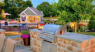 A grill is sitting on top of a stone counter in a backyard.