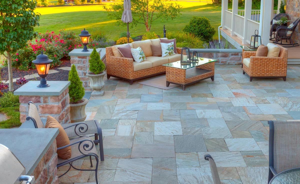 A patio with a couch , chairs , table and grill.
