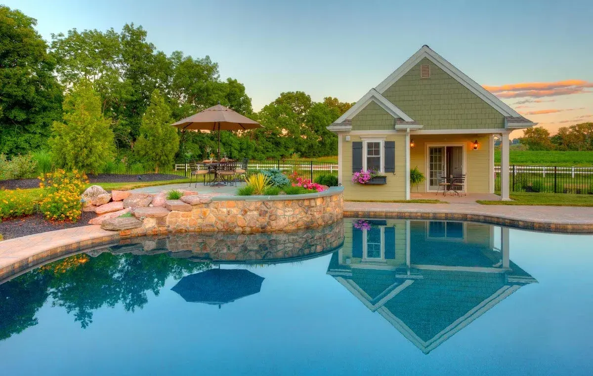 A small house is sitting next to a large swimming pool.