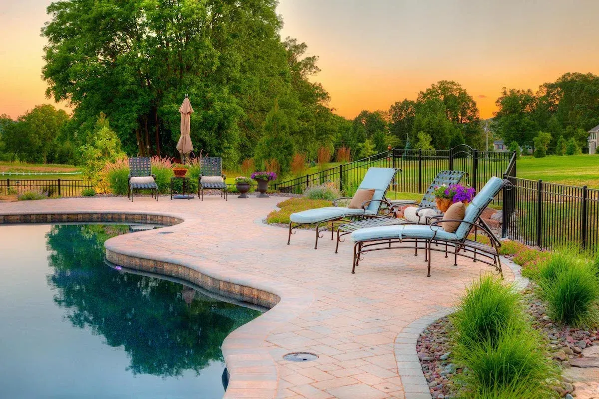 A patio with chairs and umbrellas next to a swimming pool.