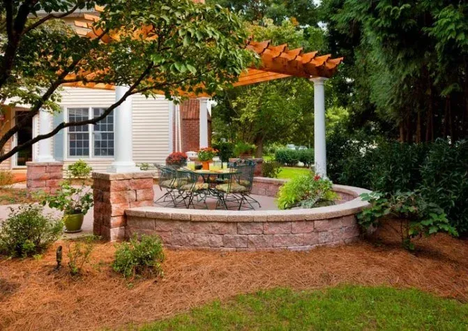 A patio with a table and chairs under a pergola in front of a house.