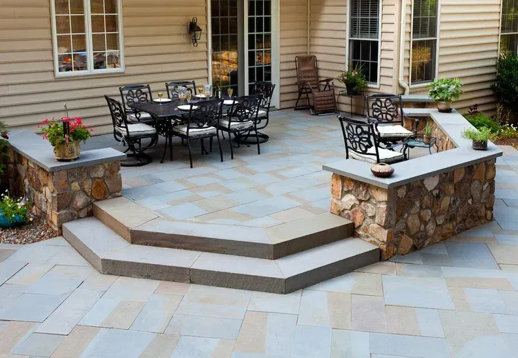 A patio with a table and chairs on it in front of a house.
