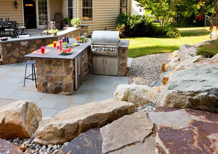 There is a grill in the middle of the patio surrounded by rocks.