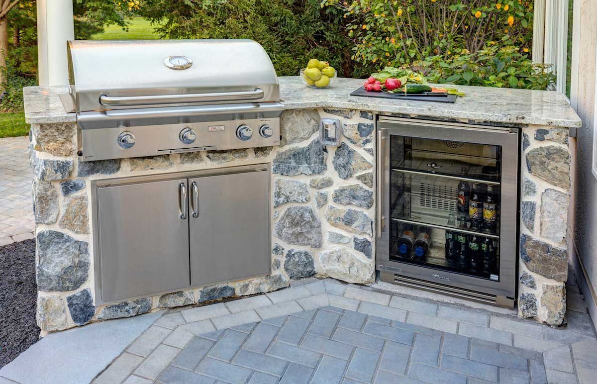 An outdoor kitchen with a grill and a refrigerator.