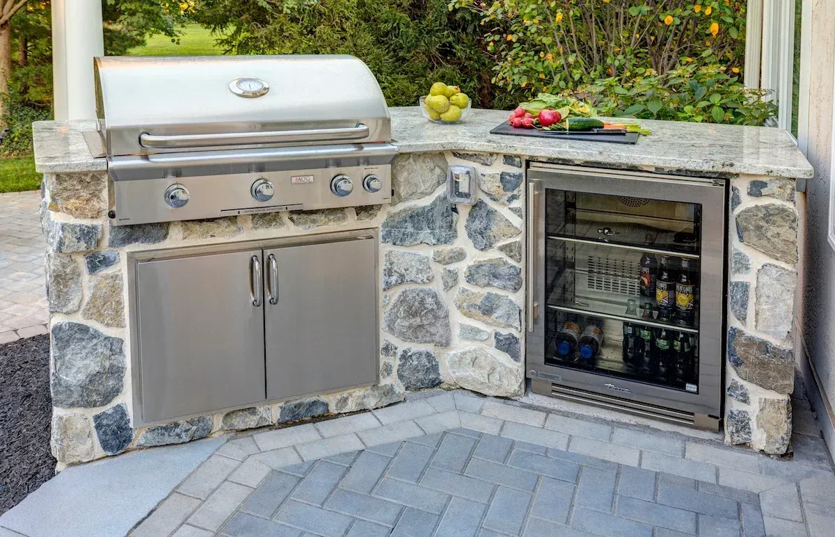 An outdoor kitchen with a grill and a refrigerator.