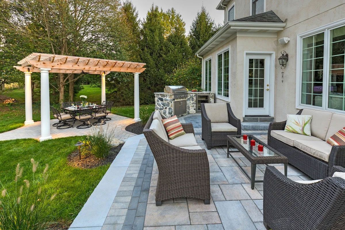 A patio with wicker furniture and a pergola in the backyard of a house.