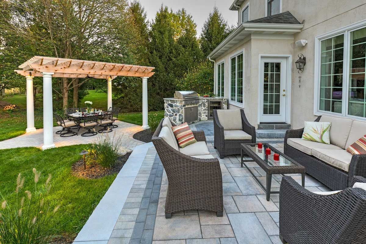 A patio with wicker furniture and a pergola in the backyard of a house.