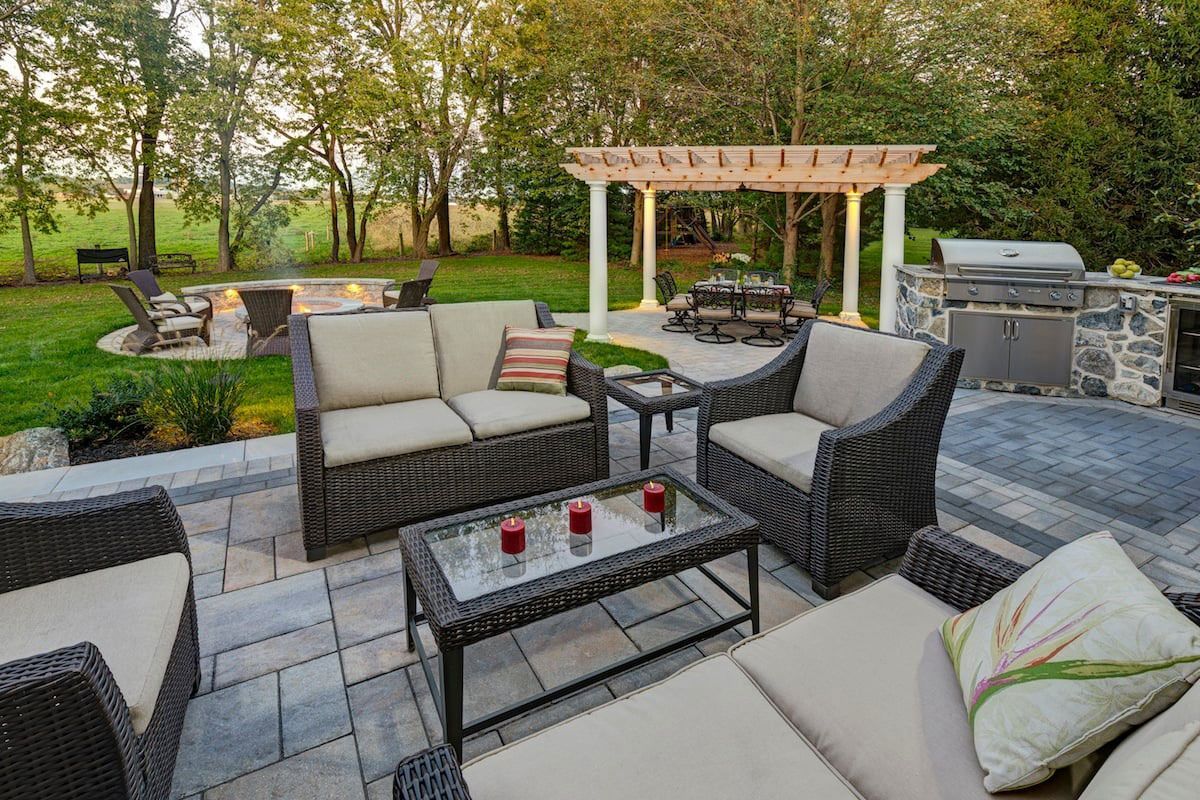 A patio with a couch , chairs , a table and a pergola.
