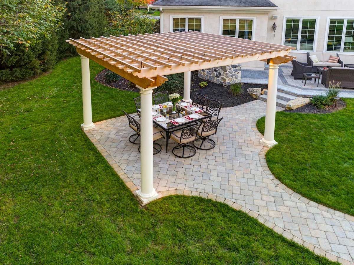 A pergola with a table and chairs underneath it in a backyard.