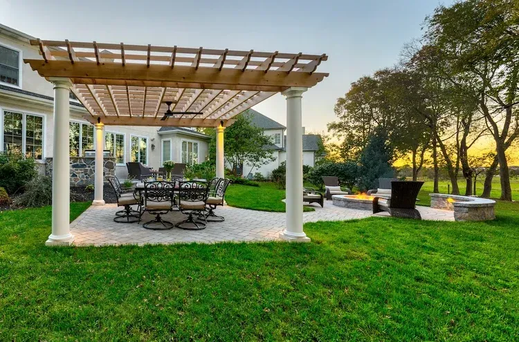 There is a pergola in the backyard with a table and chairs underneath it.